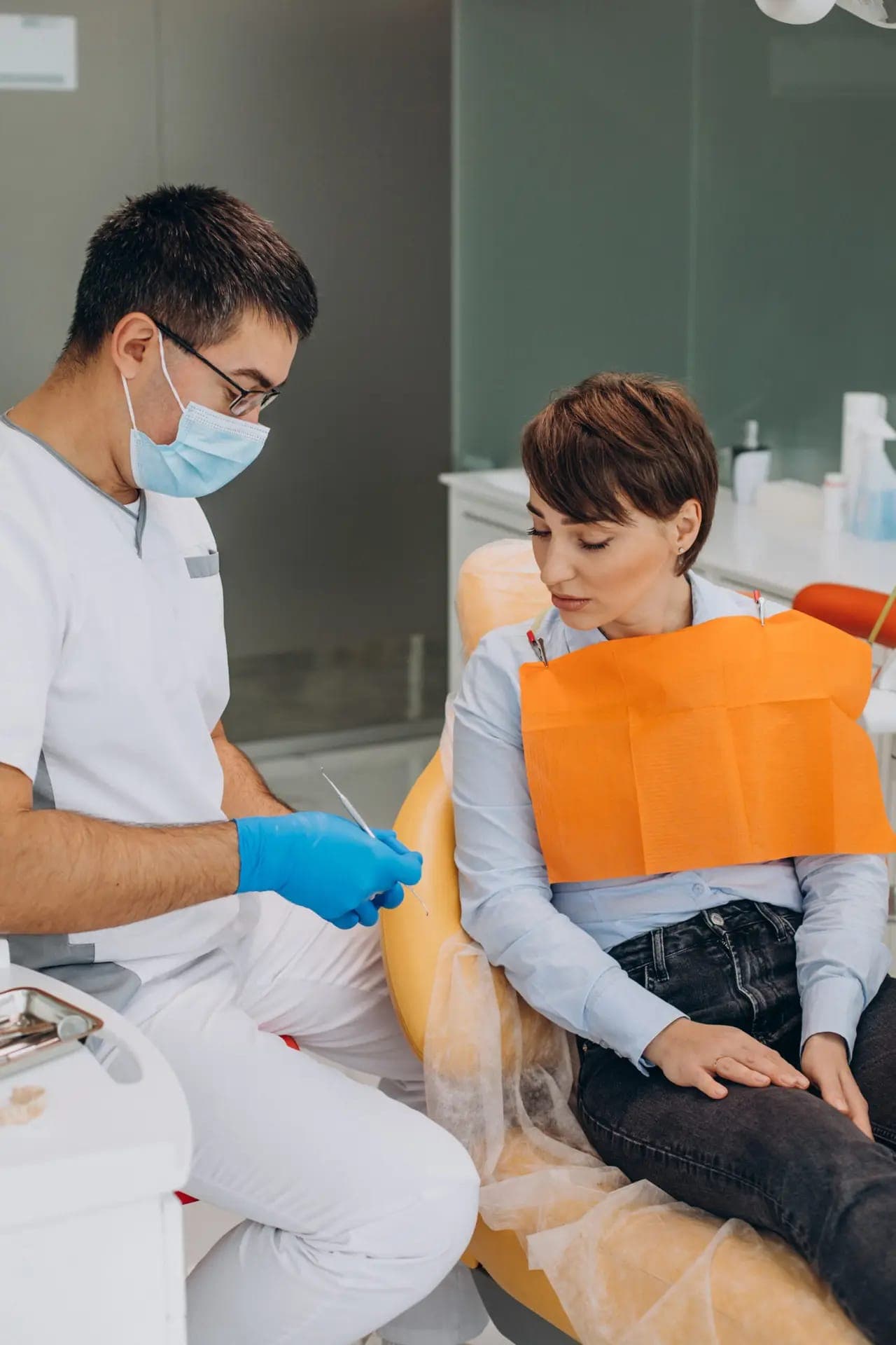 Dentist with a mask talking to a seated patient before treatment